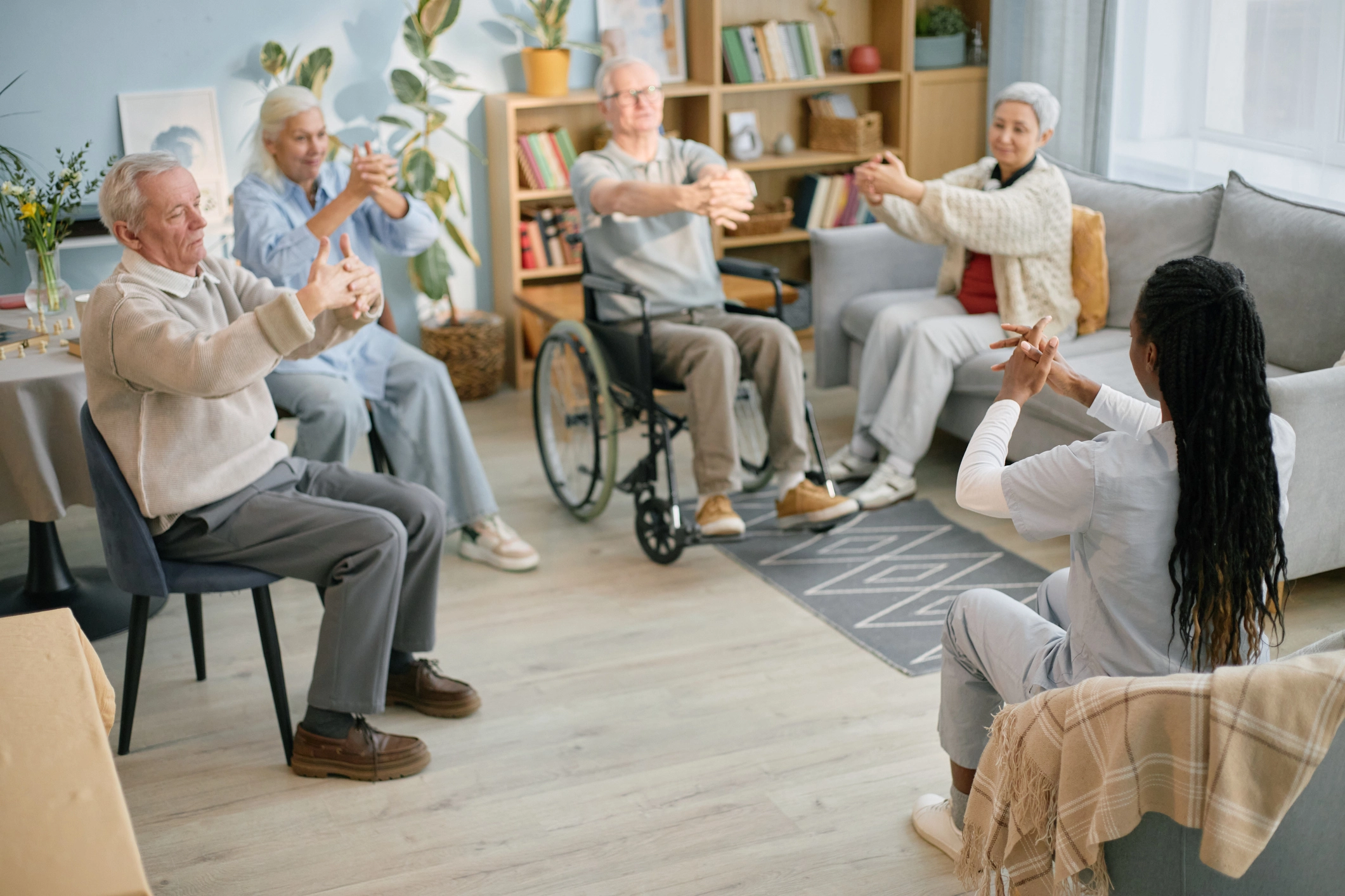 Group of seniors and a caregiver participating in a seated exercise class in a calm, well-ventilated assisted living space.