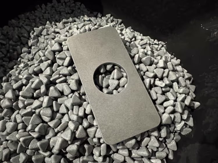 a tumbled metal part sitting on a pile of ceramic tumbling media